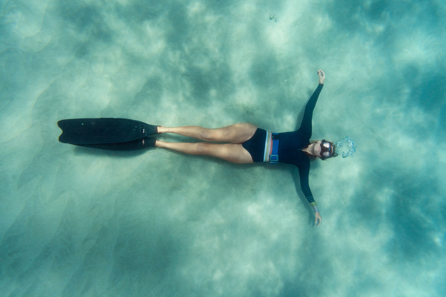 A freediver ascending toward the surface through dark blue water