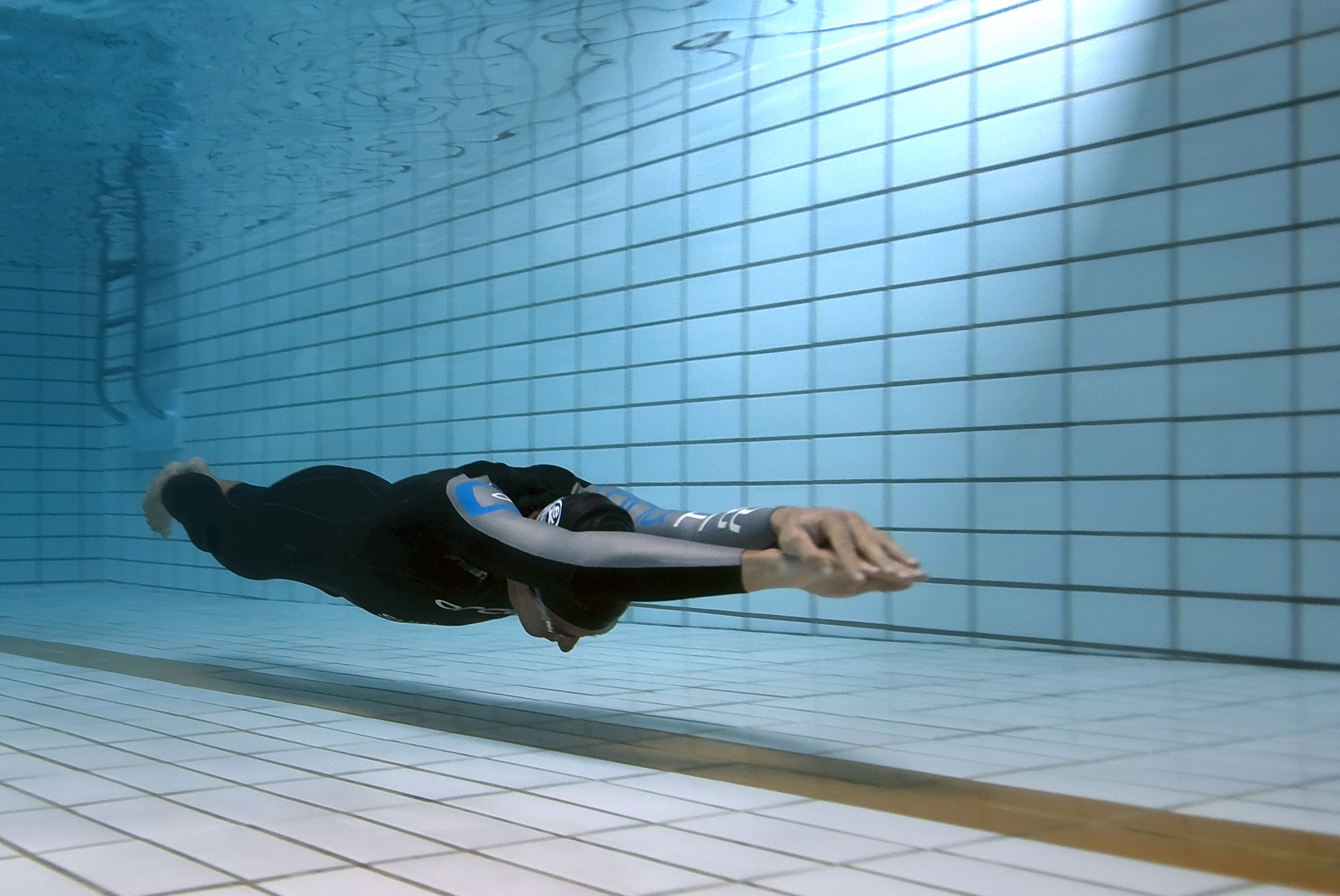 A freediver gliding underwater in a deep blue pool